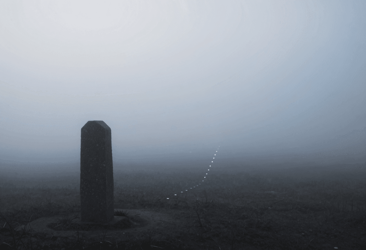 A solitary stone boundary marker stands in a dense fog at dawn, its edges dissolving into the mist